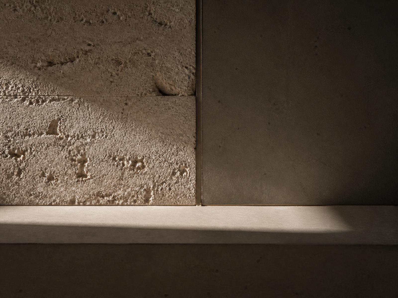 Close-up of raw travertine meeting smooth concrete, with a single beam of natural light