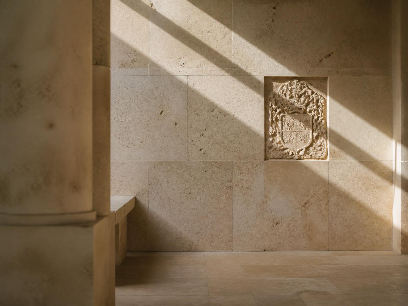 Warm natural light moving across a quiet limestone wall inside a timeless architectural space