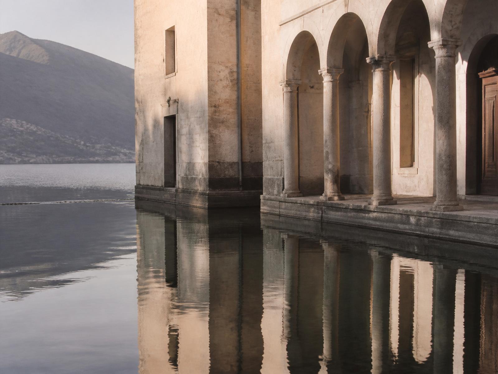 Timeless stone architecture reflected in calm water, with long shadows and soft daylight