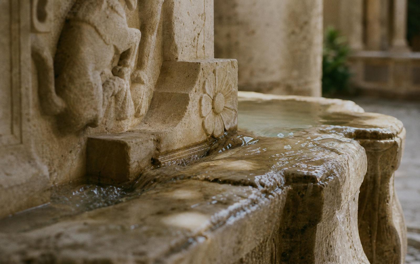 Gentle water moving across carved limestone in a quiet fountain, catching soft morning light